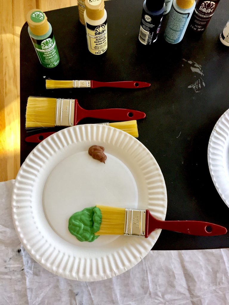 Paints arranged on folding table with paper plate palette, and paintbrushes 