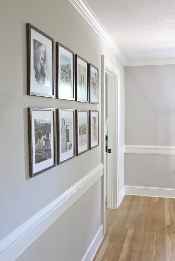Layout ideas for grid-style gallery wall in hallway | www.ourhammockhouse.com | #gallerywall #gridstylegallerywall #blackhandrail #familyphotos #whiteoakfloors #agreeablegray