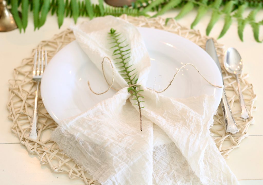 Spring place setting with white plates, vintage silver, gauze napkins tied with twine, and fern | www.ourhammockhouse.com | #springtable #eastertable #springdecor #easterdecor #ferns #gauzenapkins #vintagesilver