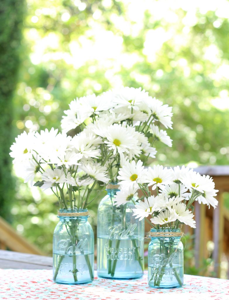 Daisies in blue mason jars with twine for centerpiece on summer picnic table | www.ourhammockhouse.com |  #daisies #centerpiece #summerdecor #springdecor #picnicdecor 