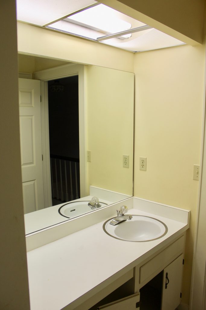 Jack-and-Jill Bathroom before image with fluorescent lights, white laminate counters, and yellow walls. 