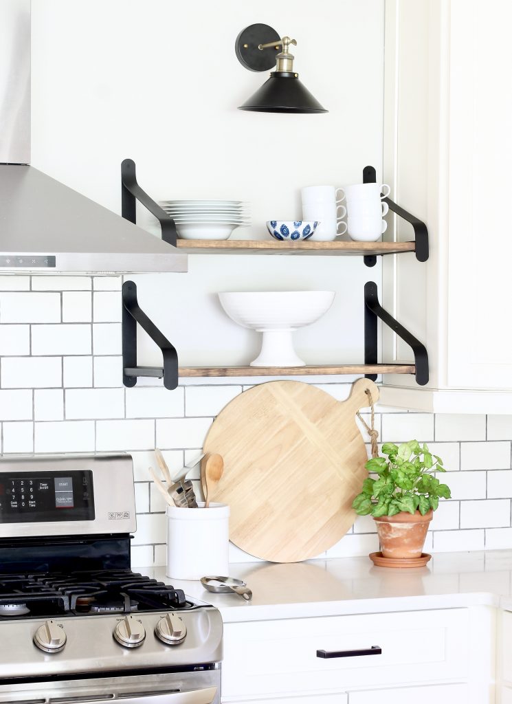 Easily turn hardwired sconces into wireless sconces! See how we installed these black and brass sconces above the open shelves in our white kitchen | www.ourhammockhouse.com | #wirelesssconce #blacksconce #wallsconce #openshelves #whitekitchen