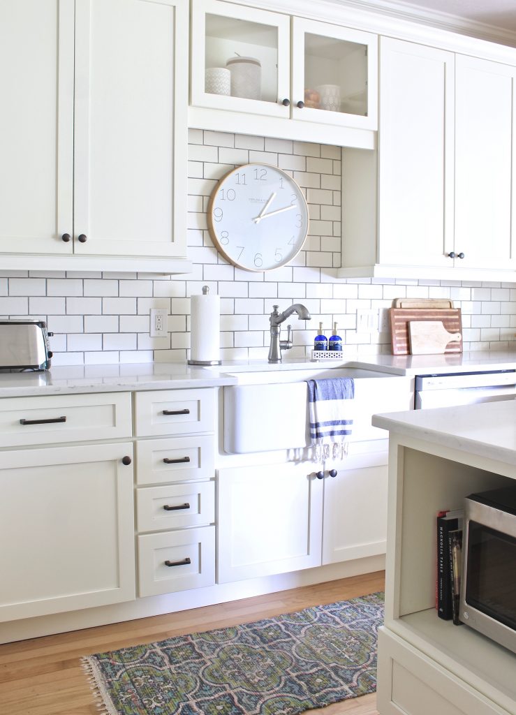 White kitchen with farm sink, large clock, and microwave under counter | www.ourhammockhouse.com | #whitekitchen